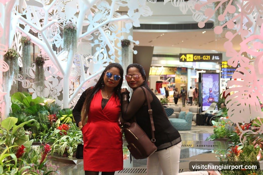 Two women posing in a mall with plants and decorative tree