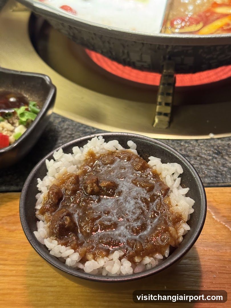 Bowl of Rice with Sauce and Hot Pot in Background