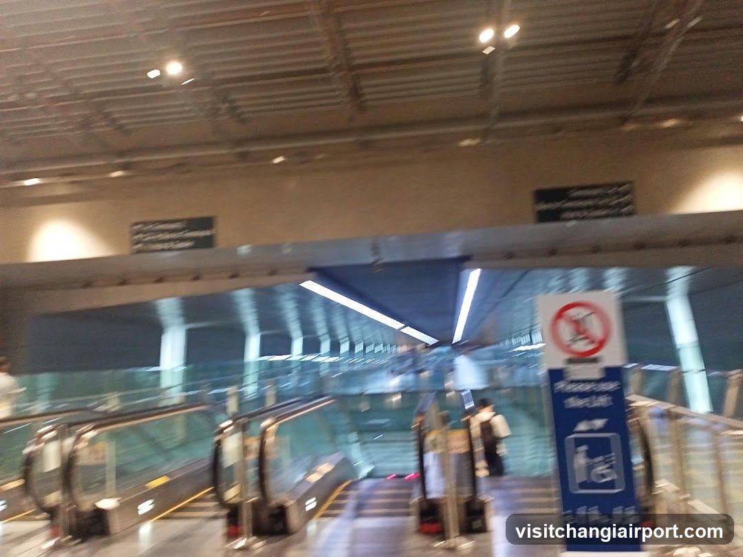Interior view of a subway or transit station platform with escalators leading down, glass railings, and signage indicating 'Please Use Elevator' and no smoking rules. A person is visible near the elevator.