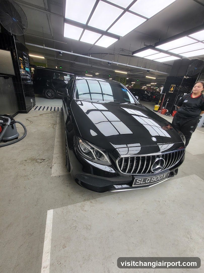 A black Mercedes-Benz E-Class is parked inside a car detailing shop, with bright overhead lighting and cleaning equipment visible in the background.