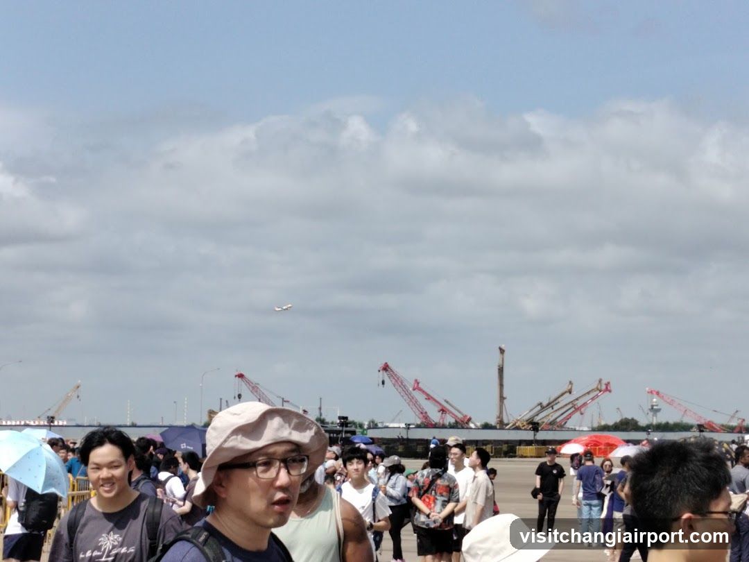 Crowd at an outdoor event with cranes in the background