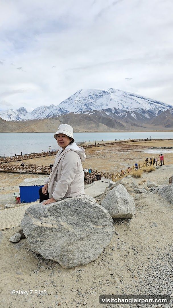 Woman sitting on rock near lake with mountains in background